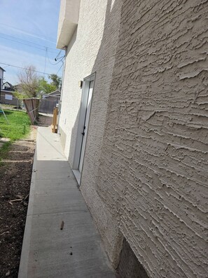 A residential building with a textured exterior wall, a concrete pathway, and a wooden fence in the background. - The Cozy Corner Home (Winnipeg)