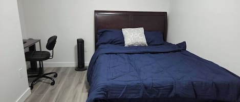 Un dormitorio con una cama, un escritorio, una silla y un ventilador de pie.