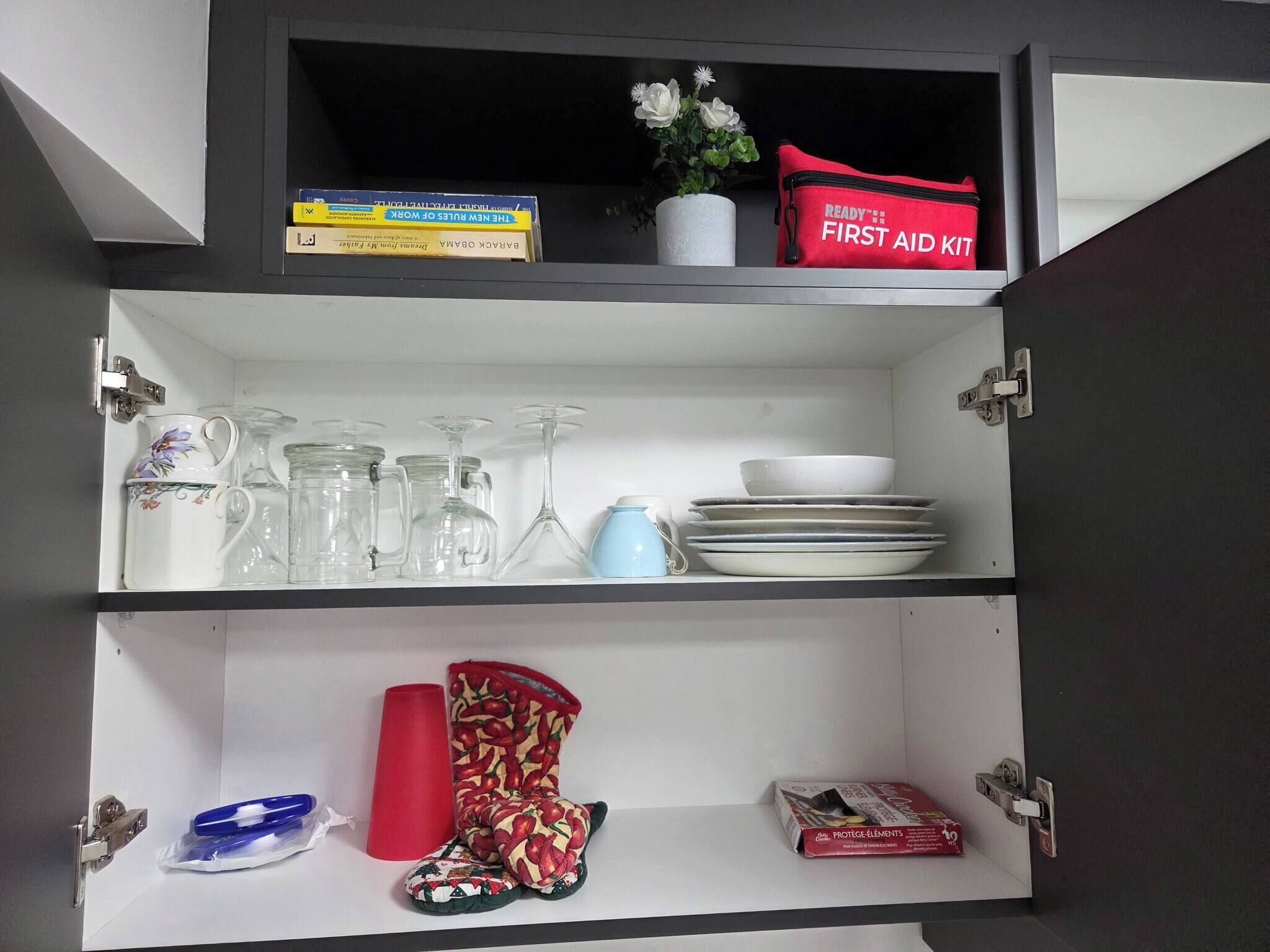 A cabinet with shelves containing kitchenware, a first aid kit, and a decorative item.