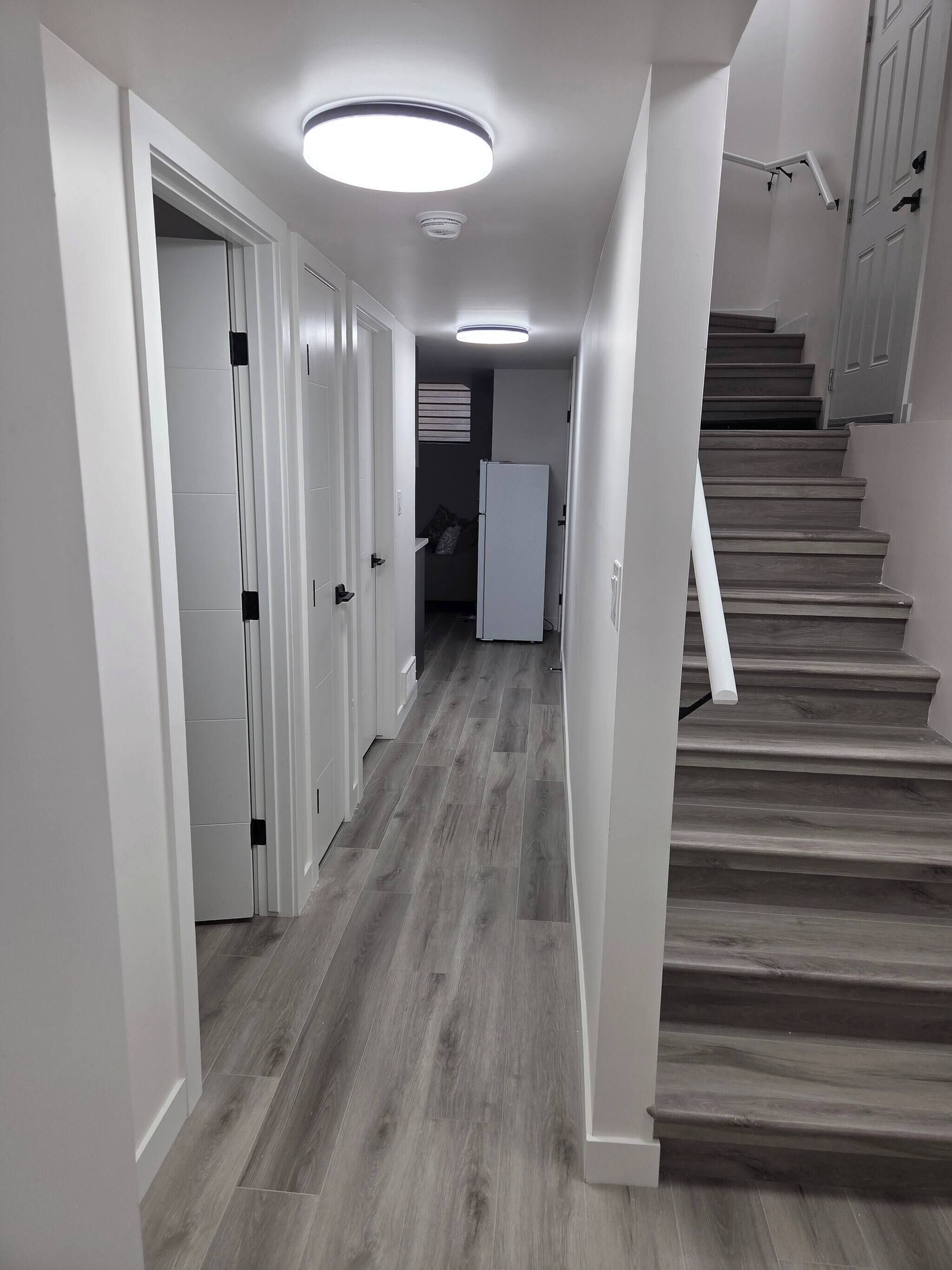 Un couloir avec un escalier en bois, des murs blancs et un luminaire au plafond.