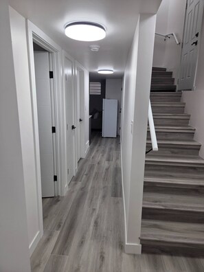 Un pasillo con escaleras de madera, paredes blancas y una lámpara en el techo.