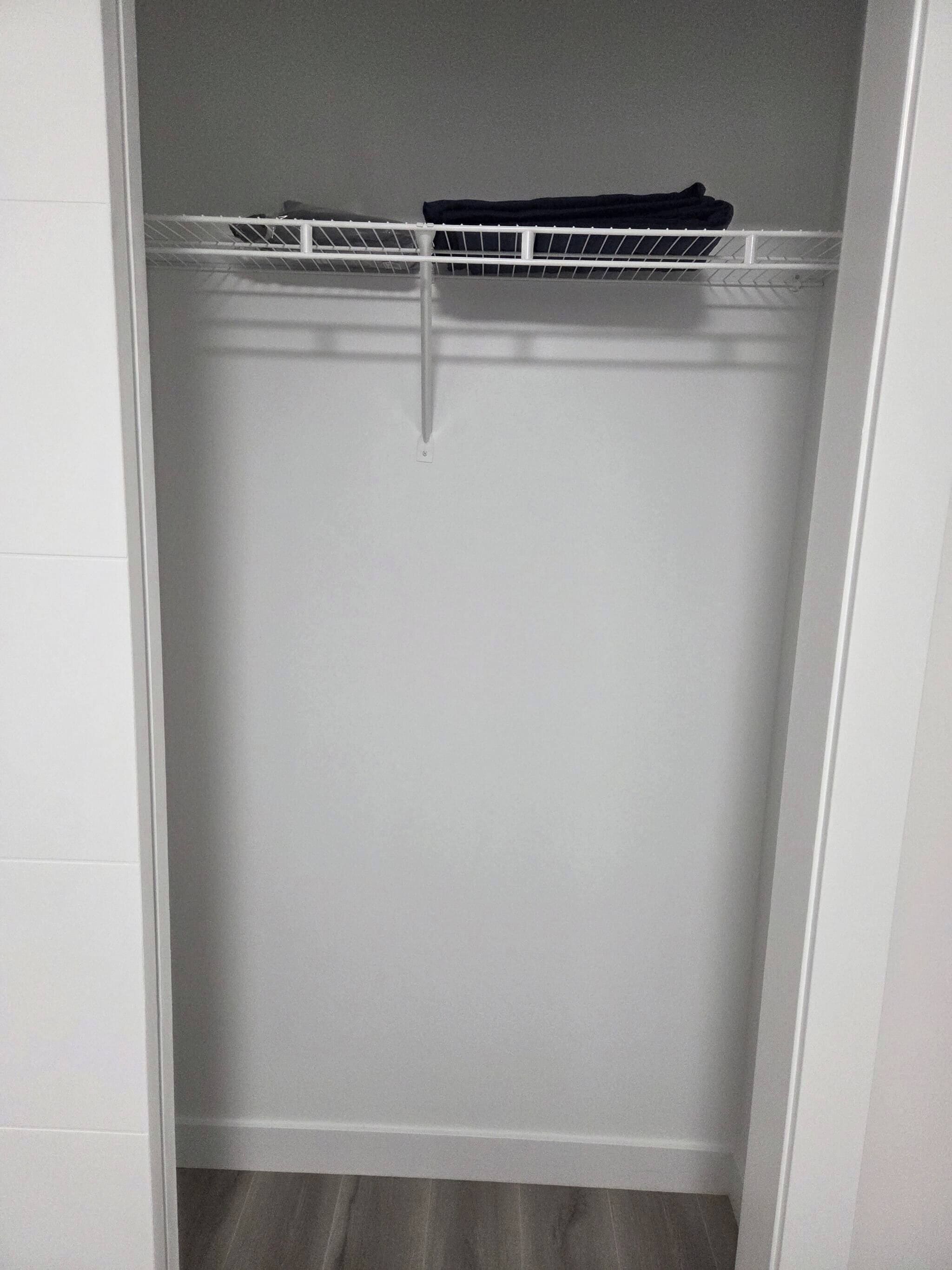 Ein weißer Kleiderschrank mit einer Metallablage oben und einer weißen Tür.