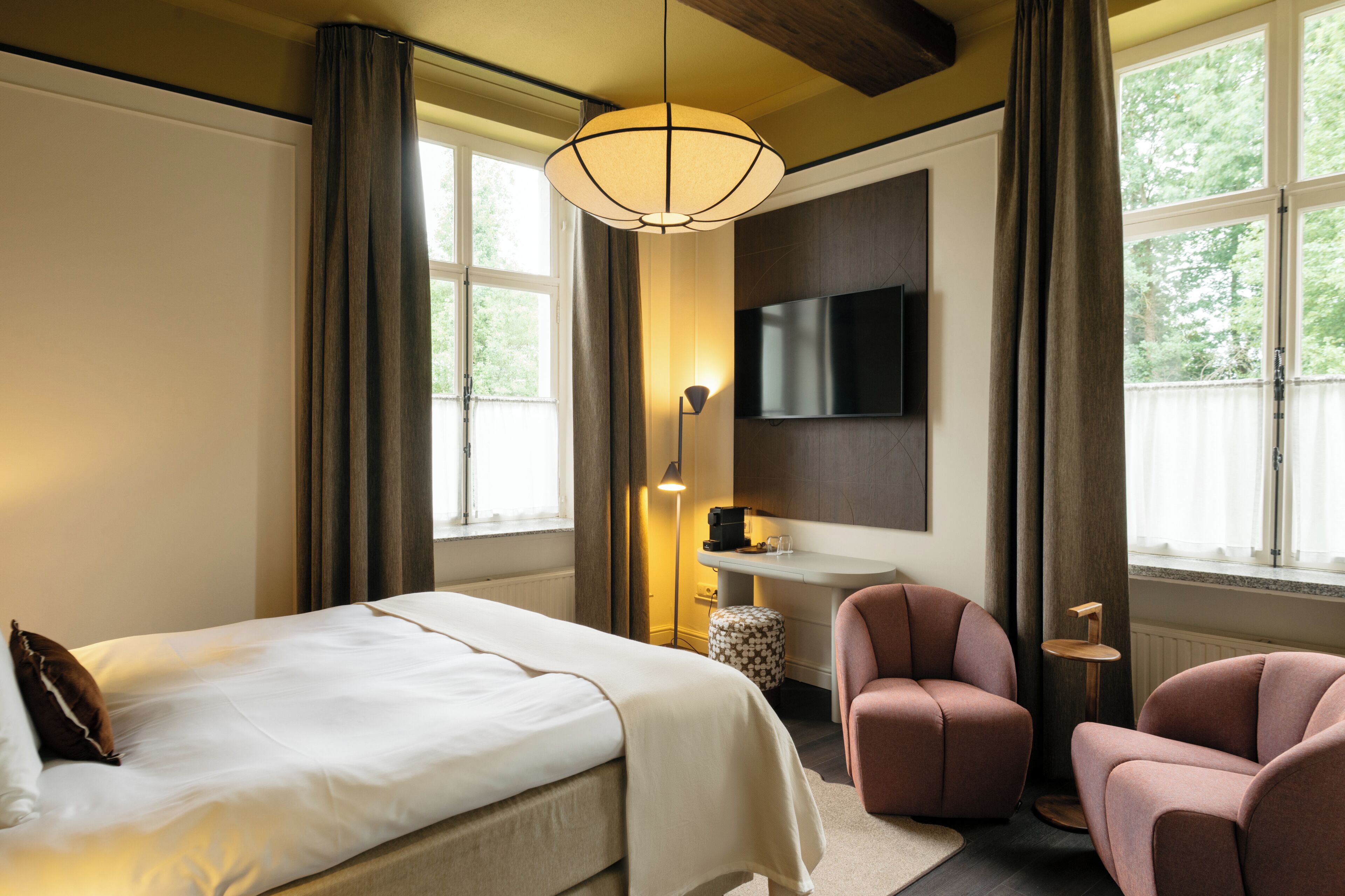 Ein Hotelzimmer mit Bett, Schreibtisch, Stuhl, Fernseher und einem Fenster mit Vorhängen.