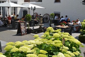 An outdoor café with tables and chairs, surrounded by greenery and a white building. - Kasteel Doenrade (Doenrade)