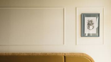 A neatly made bed with white linens and a brown headboard. There is a bedside table with a lamp and a framed picture on the wall above.