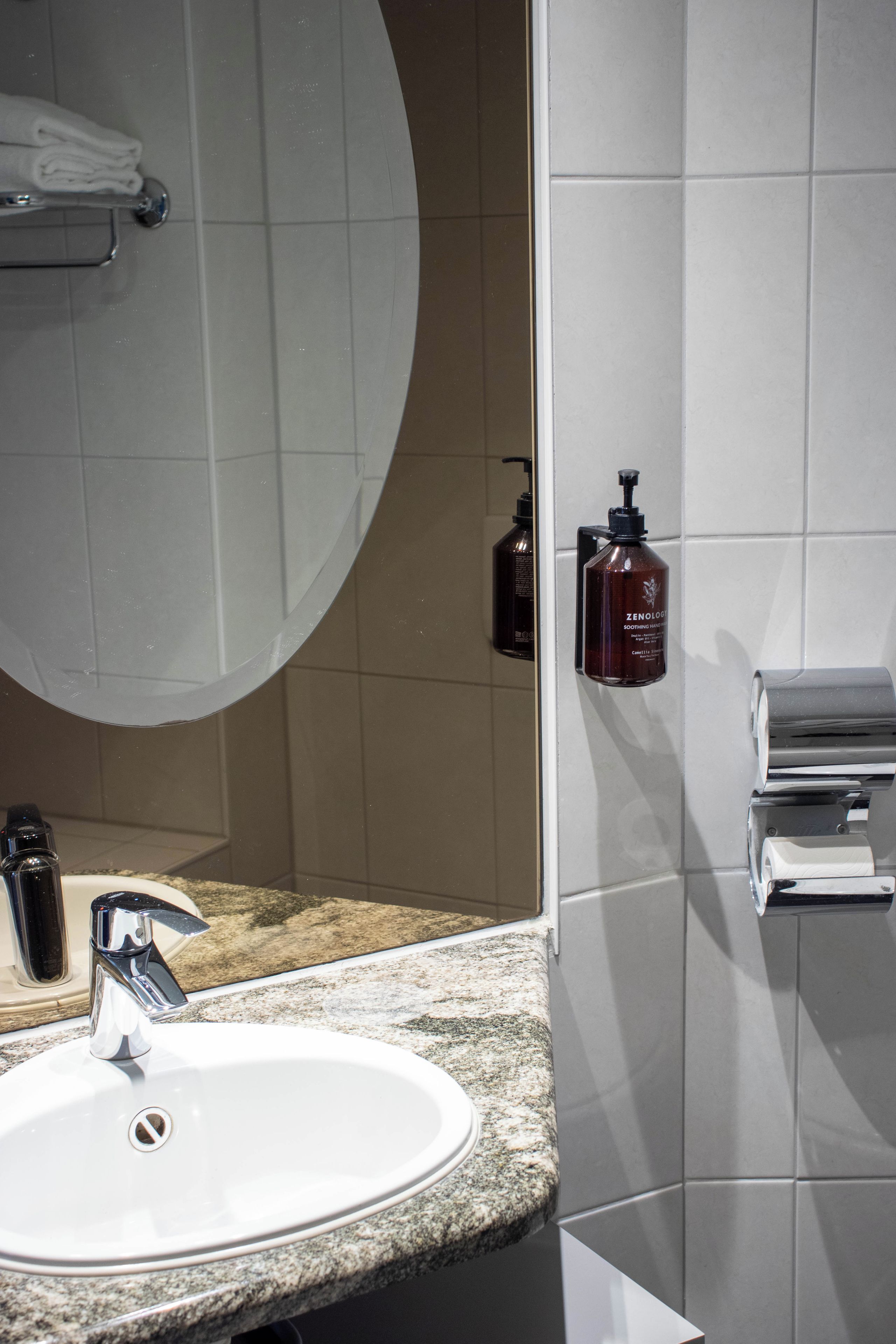 A bathroom with a sink, mirror, towel rack, and toiletries.