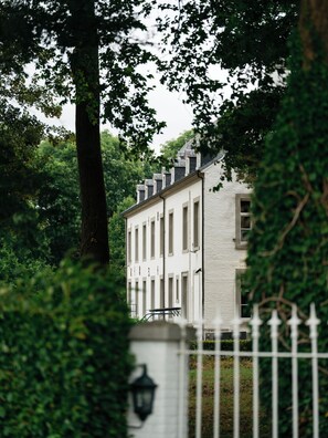 A white building with a symmetrical facade, surrounded by lush greenery and a white fence.