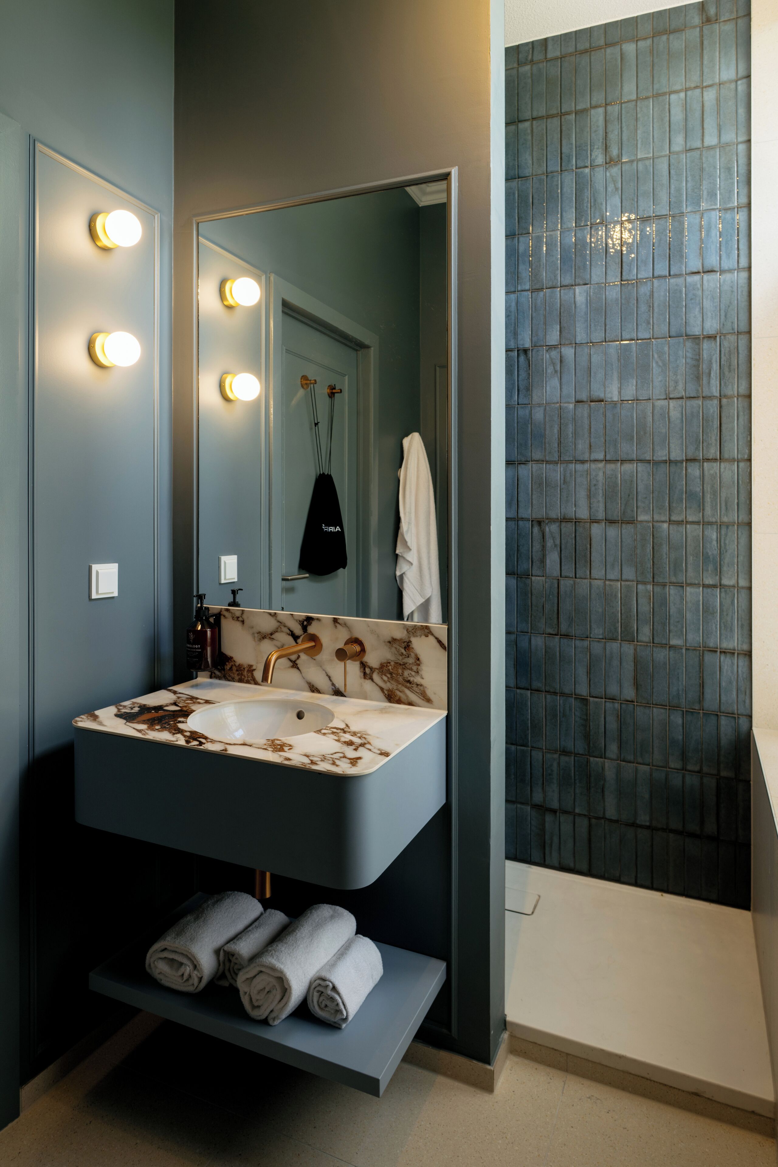 Un baño con lavamanos de mármol, un espejo con luces, toallero y pared con azulejos azules.