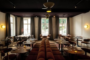 A restaurant with multiple dining tables and booths, large windows with curtains, and pendant lighting. - Kasteel Doenrade - digital check-in, key by email or SMS (Doenrade)