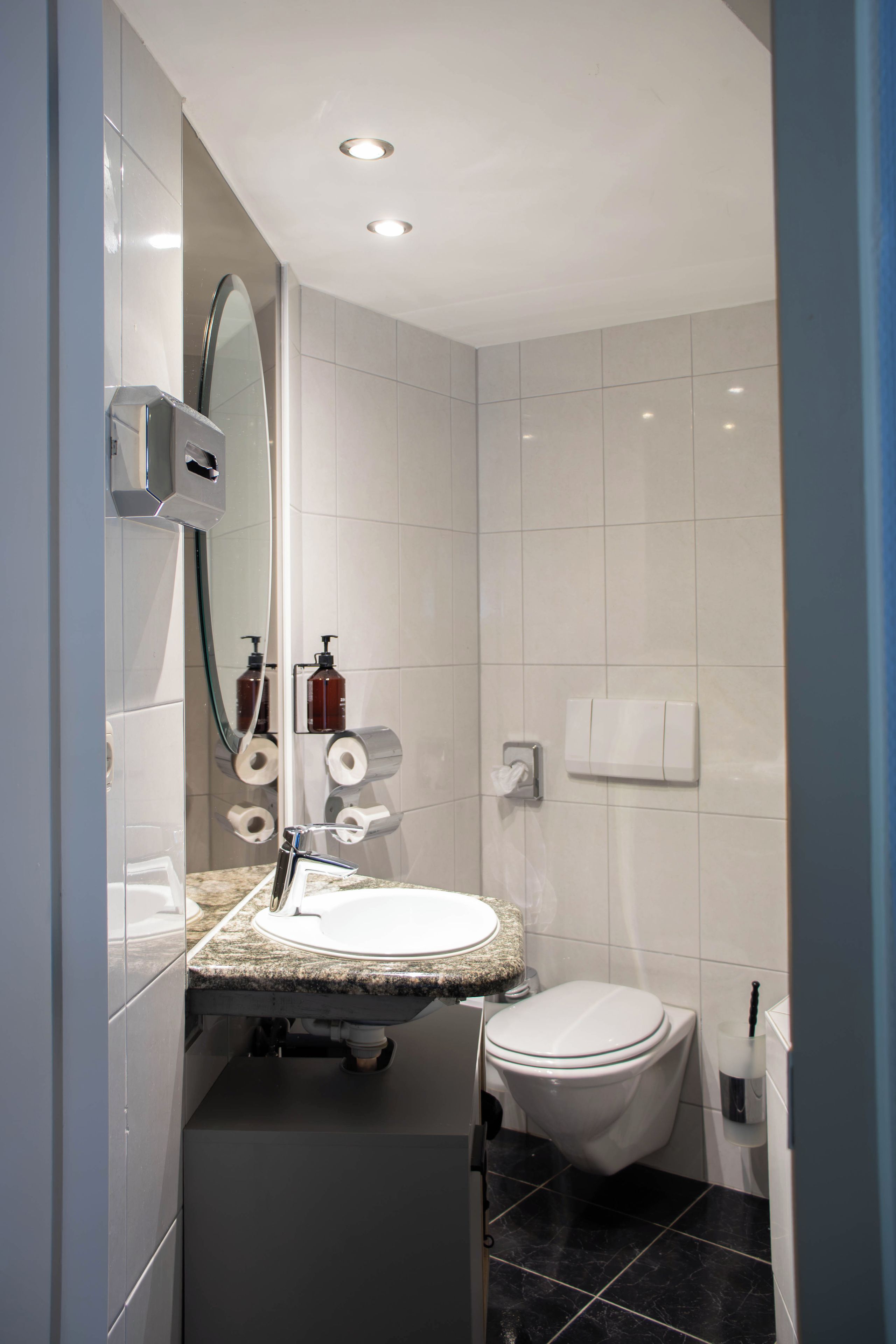 A modern bathroom with a white sink, mirror, toilet, and shower area.