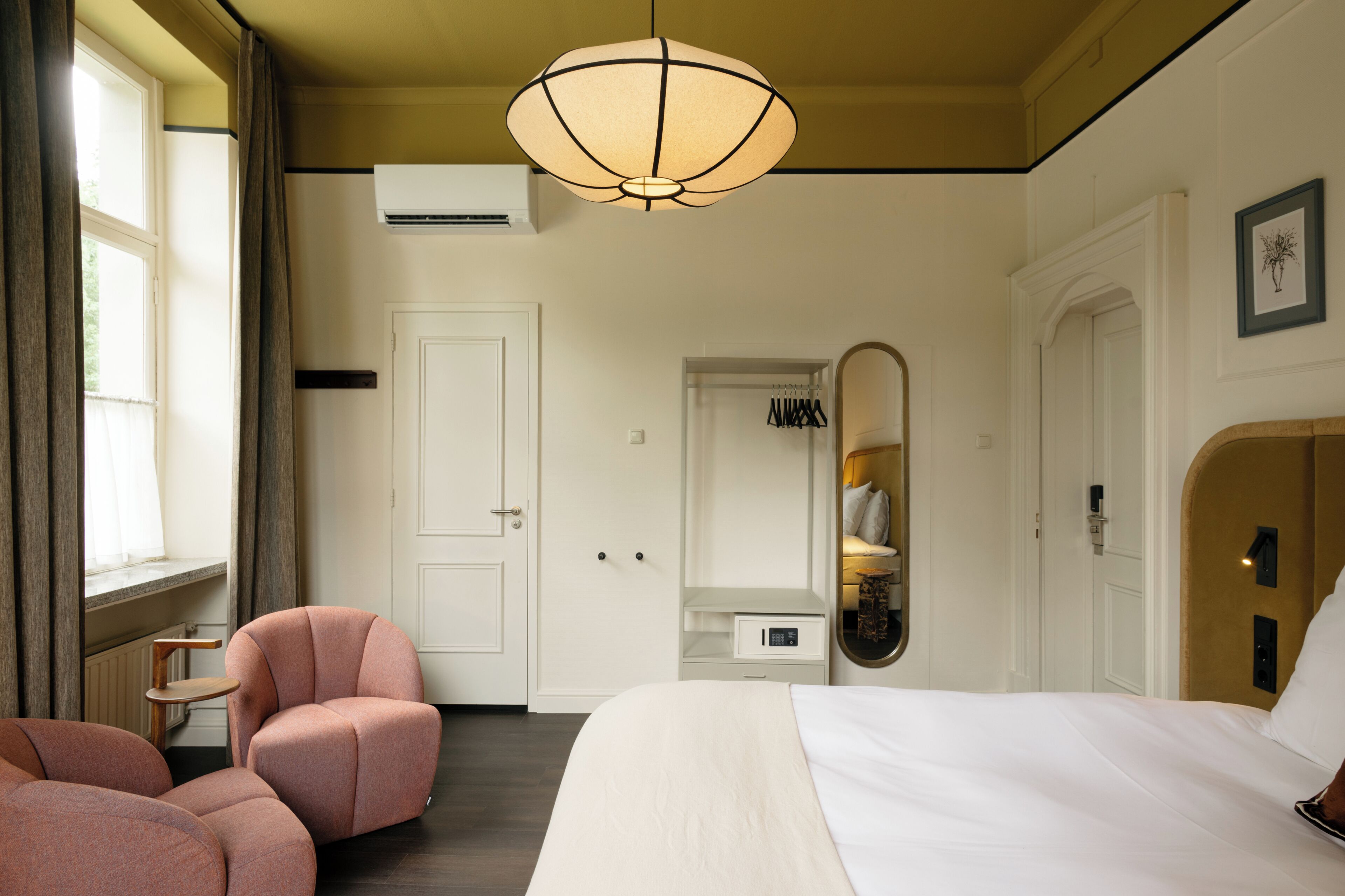 Habitación de hotel con cama, una silla, armario, espejo y lámpara colgante.