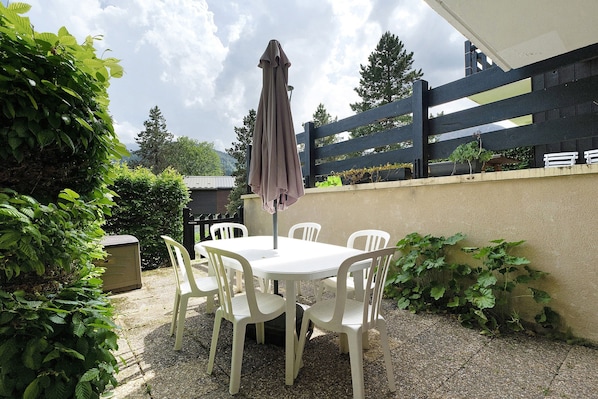 Une terrasse extérieure avec une table et des chaises blanches, un parasol violet et une clôture noire.
