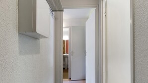 Un pasillo estrecho con paredes blancas y suelo de madera que conduce a un baño con inodoro y lavamanos.
