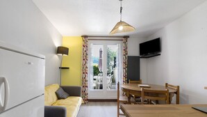 Una habitación compacta con sofá, mesa de comedor, televisor y ventana con cortinas.
