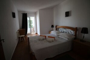 Ein Schlafzimmer mit einem Bett, zwei Nachttischen, einem Sessel und einem Fenster mit Vorhängen.
