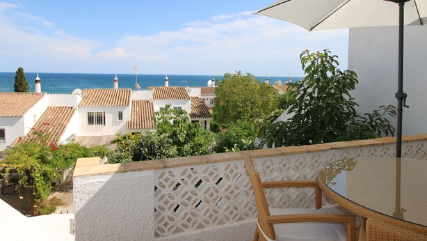 A balcony with a wicker chair and a table, overlooking a coastal town with terracotta rooftops and a view of the sea. - CASA 8 - Sea View T3 (Luz)