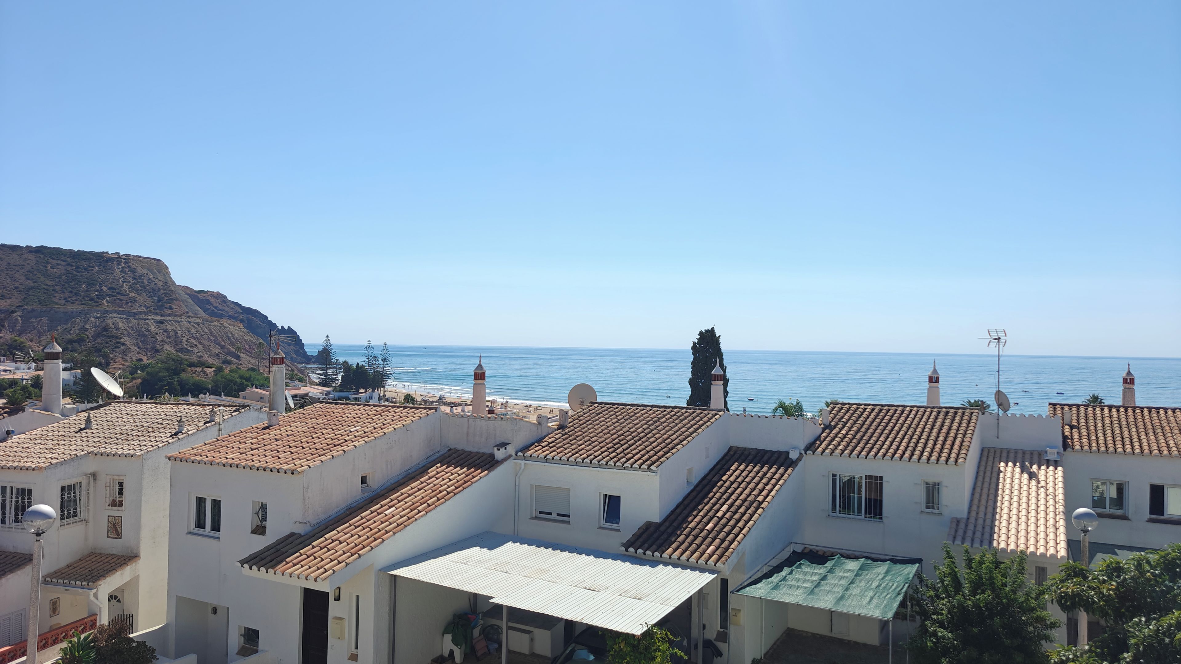 Un área residencial costera con techos de tejas de color terracota, un faro destacado y una vista despejada del mar.