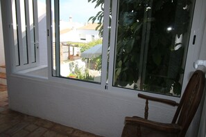 Ein Zimmer mit einem großen Fenster, einem Holzstuhl und Blick auf einen Garten und Gebäude.