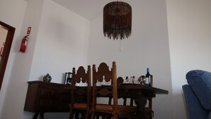 A dining area with a table, chairs, a hanging light fixture, and a fire extinguisher on the wall. - CASA 8 - Sea View T3 (Luz)