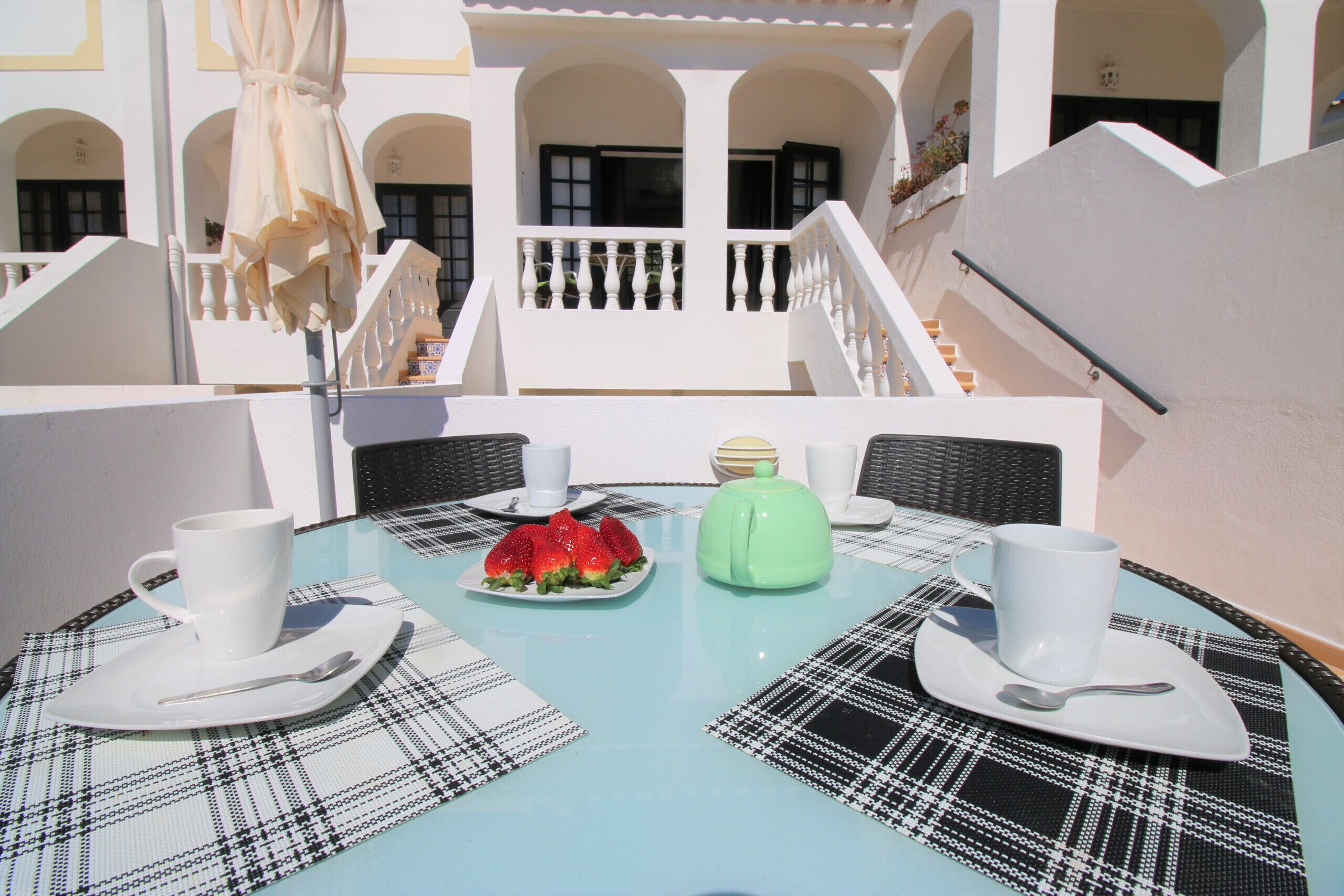 Une table dressée avec une assiette de fraises, une théière verte et des tasses et soucoupes blanches.