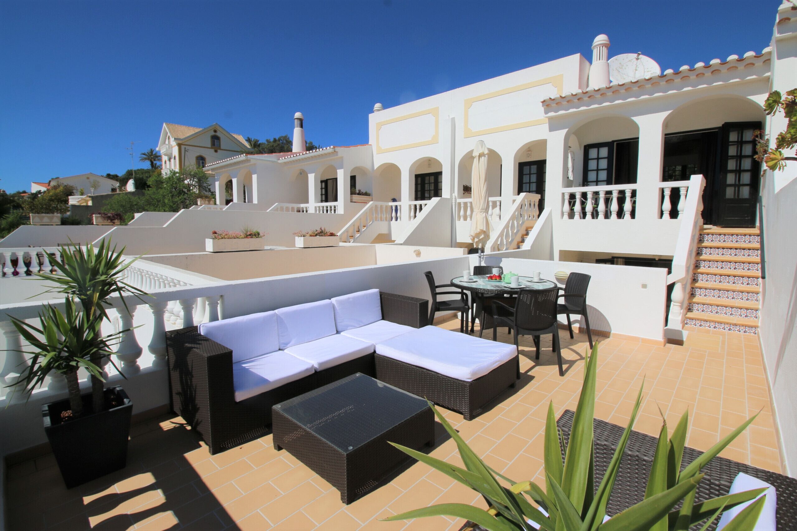 A rooftop terrace with a sofa, dining table, chairs, and potted plants.