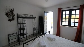 Ein Zimmer mit einem Bett, einer Metallregalkonstruktion, einer Tür und einem Fenster mit Vorhängen.