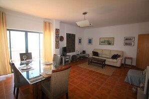 Una sala de estar con una mesa de comedor, sillas, un sofá, un televisor y obras de arte en las paredes.