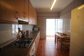 Eine Küche mit Holzschränken, einem Gasherd, einem Kühlschrank und einem Essbereich mit Tisch und Stühlen.