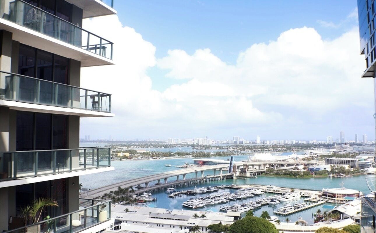 A high-rise building with multiple balconies overlooking a marina and a bridge.