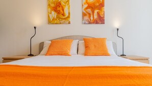 Ein Bett mit orangefarbener Decke, zwei Kissen und zwei Wandlampen.