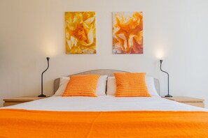Ein Bett mit orangefarbener Decke, zwei Kissen und zwei Wandlampen.
