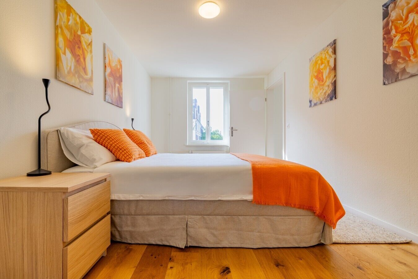 A bedroom with a bed, a nightstand, a dresser, and a window with a view.