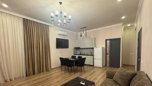 Un saló amb un sofà, una taula de centre, una taula de menjador amb cadires, una zona de cuina i un penjador.