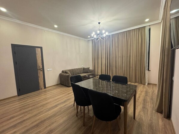 A room with a dining table, chairs, a sofa, and curtains.