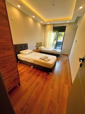 A hotel room with two beds, wooden flooring, and a view of the outdoors. - Peaceful Holiday Villas-luxury (Serik)