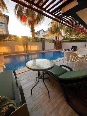 A poolside area with a glass table, lounge chairs, and a pergola structure. - Peaceful Holiday Villas-luxury (Serik)