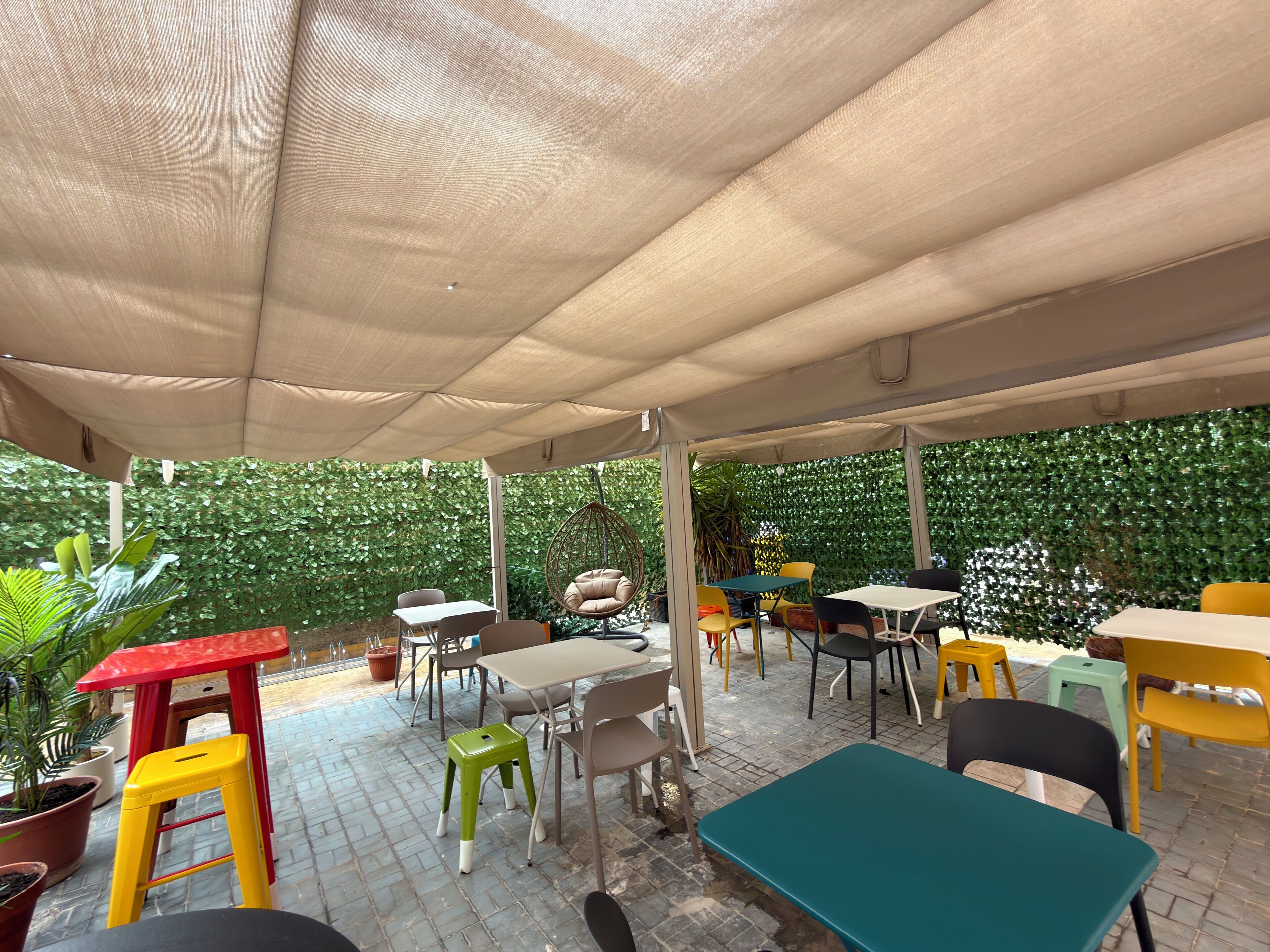 Un patio al aire libre con mesas y sillas, un sillón colgante y plantas en macetas.