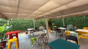 Un espace extérieur aménagé en terrasse, avec des tables et des chaises, un fauteuil suspendu et des plantes en pot.