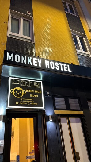 Un edificio con un cartel que dice 'MONKEY HOSTEL MILANO' y un logotipo de mono.
