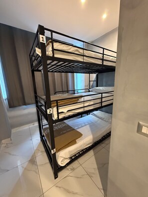 A bunk bed with three levels, numbered 1, 2, and 3, in a room with a tiled floor and a window with curtains.