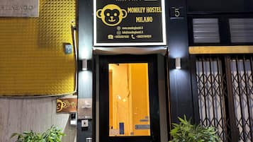 The exterior of the Monkey Hostel in Milano, featuring a prominent sign with a monkey logo, a number 5, and contact information.