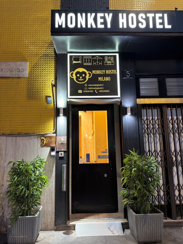The exterior of the Monkey Hostel in Milano, featuring a prominent sign with a monkey logo, a number 5, and contact information.