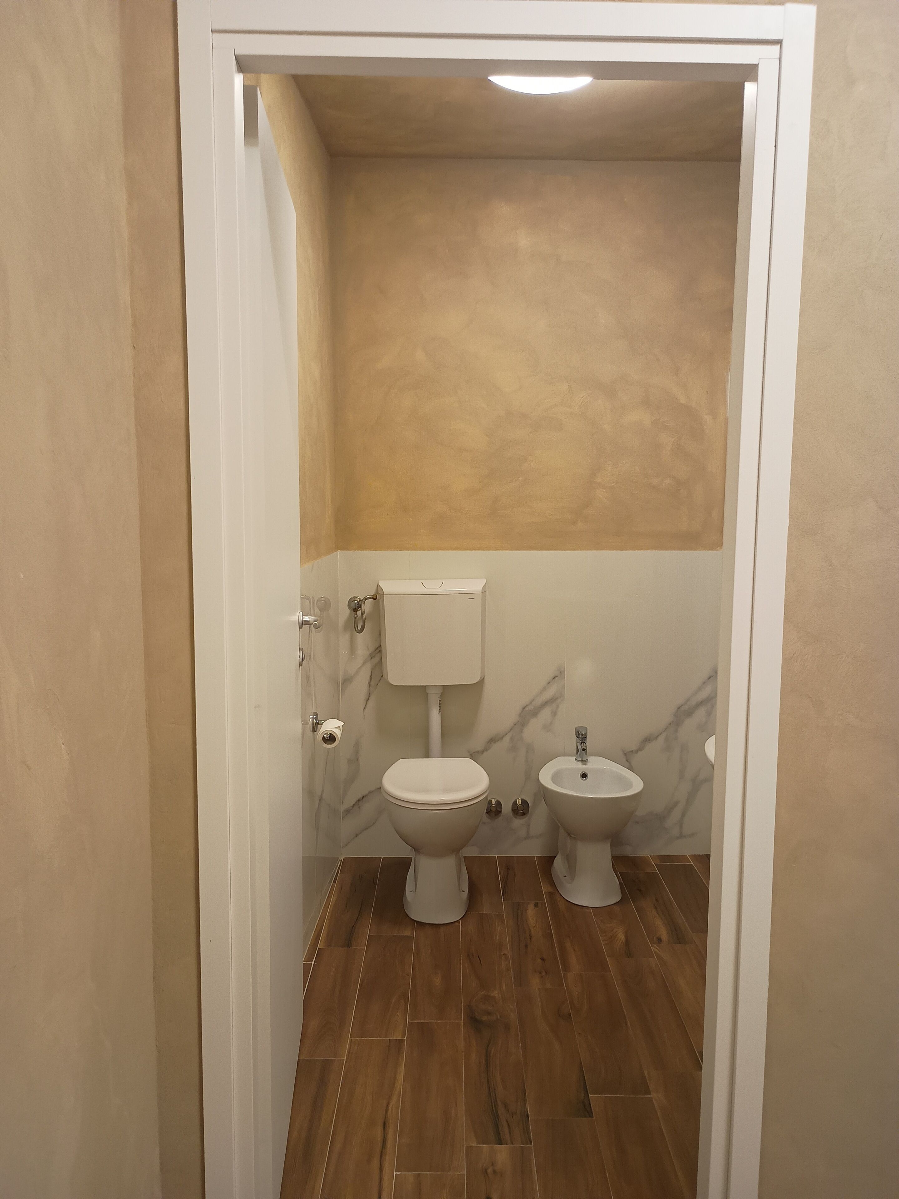 A bathroom with a toilet, bidet, and a marble wall.