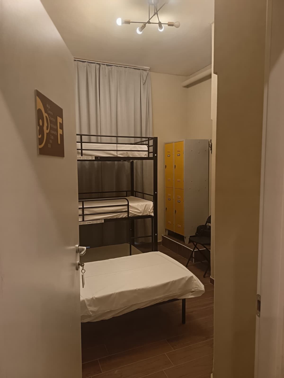 Habitación tipo dormitorio con literas, un escritorio, una silla y una serie de taquillas amarillas.
