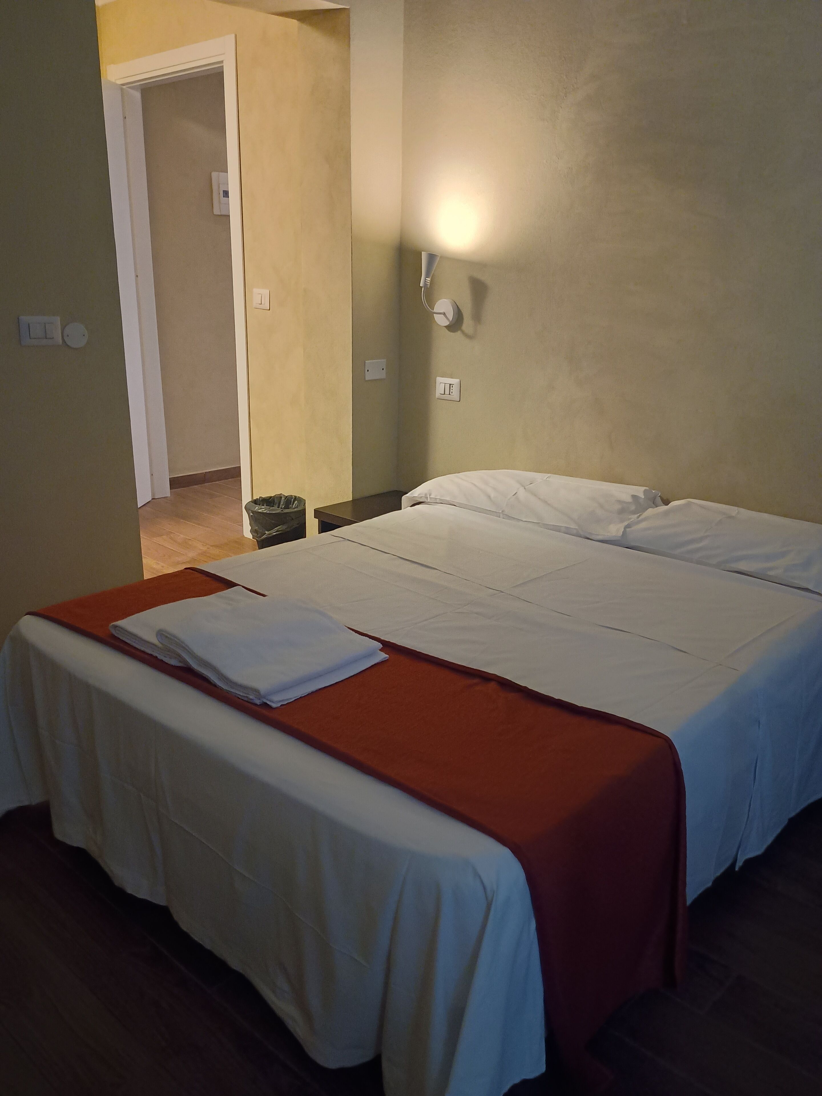 Una habitación de hotel con cama, mesita de noche y lámpara fijada a la pared.