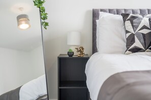 A neatly made bed with a geometric patterned pillow, a bedside lamp, a small plant, and a decorative golden figure on a black nightstand. - 10 minute walk to Anfield | FREE Parking | Sleeps 4 | Contractor Friendly | WIFI (Liverpool)