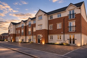 A row of modern multi-story residential buildings with uniform architecture, featuring balconies and a paved driveway. - 10 minute walk to Anfield | FREE Parking | Sleeps 4 | Contractor Friendly | WIFI (Liverpool)