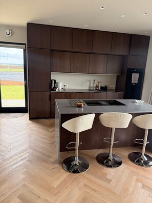 A modern kitchen with dark wood cabinets, a stainless steel island, and three bar stools. - Charming Holiday House in Álftarnes Iceland With Scenic Views (Garðabær)