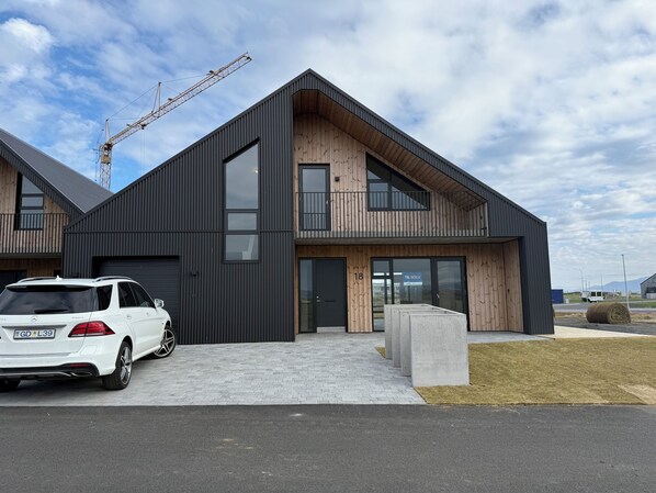 A modern two-story building with a large garage door, a visible address number, and a parked white car. - Charming Holiday House in Álftarnes Iceland With Scenic Views (Garðabær)