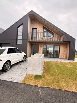 A modern building with a car parked in front, a balcony, and a large window. - Charming Holiday House in Álftarnes Iceland With Scenic Views (Garðabær)